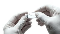 Gloved hands opening a small glass medical vial, close-up shot for healthcare, pharmaceutical, and laboratory research concepts.