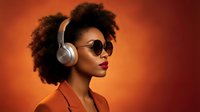 Young African American woman with curly afro hair wearing wireless headphones and sunglasses against vibrant orange gradient background for music and lifestyle content.