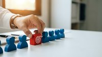 Business professional selecting red target cube from blue figures representing strategic leadership and team management in corporate environment.