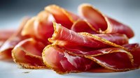 Thinly sliced cured meat prosciutto ham arranged on white surface. Premium Italian delicatessen cold cuts for charcuterie boards and gourmet cooking.