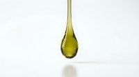 Golden olive oil drop falling from spoon against white background. Natural cooking ingredient for culinary recipes and healthy Mediterranean diet preparation.