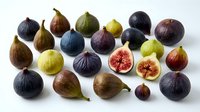 Fresh figs in various stages of ripeness arranged on white background, showing whole fruits and cross-sections with pink flesh. Use for food styling, culinary content, healthy eating campaigns.