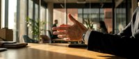 Professional businessman extending hand for handshake in modern office meeting room with natural lighting and glass walls for business partnership.