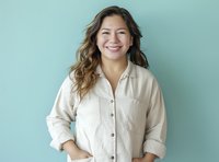Young Hispanic woman with long wavy brown hair wearing casual white button-up shirt smiling genuinely against turquoise background, expressing joy and confidence.