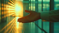 Silhouette of outstretched hand reaching towards bright sunburst through window, creating dramatic lighting effect against teal background. Concept of hope and aspiration.