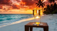 Two champagne glasses on wooden table at tropical beach during golden sunset with palm trees and ocean waves creating romantic atmosphere for celebration.