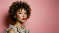 Young African American woman with curly afro hair and red lipstick wearing ruffled top against pink background for fashion and beauty concepts.