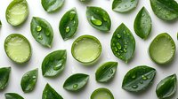 Fresh cut limes and green citrus leaves with water drops scattered on white background, flat lay pattern composition for food and beverage design.