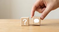 Hand placing wooden cube with speech bubble next to question mark block on desk representing communication, problem solving and customer support concepts.