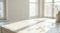Empty marble countertop surface in bright modern kitchen with natural sunlight streaming through windows creating soft shadows for product display.