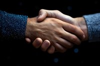 Close-up of diverse business handshake between African and Caucasian partners against dark background with bokeh lights, symbolizing trust and cooperation.