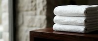 Stacked white towels on wooden surface with blurred background, suitable for spa, hotel, and wellness marketing materials.