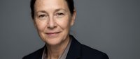 Mature woman with light skin tone and brown hair wearing dark blazer against neutral gray background, suitable for corporate, business, and professional portraits.
