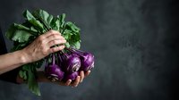 Fresh purple cabbage with green leaves held in hand against dark background, suitable for organic food, healthy eating, and farm produce marketing.