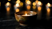 Ceramic bowl with burning candle creating warm ambient lighting against blurred golden bokeh lights background for relaxation and meditation atmosphere.