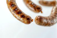 Grilled bratwurst sausages with crispy brown crust and grill marks on white background, close-up macro shot showing juicy meat texture and caramelization.