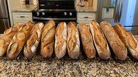 Fresh crusty French baguettes lined up on marble kitchen counter, golden brown artisanal bread loaves with crispy crust and rustic texture, homemade bakery display.