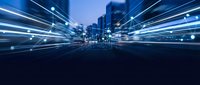 Abstract blue light trails streaking through modern city skyline at night creating dynamic motion blur effect for technology and speed concepts.