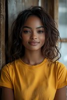 Young mixed-race woman with curly hair wearing yellow t-shirt smiling at camera in casual indoor portrait for lifestyle and fashion content.