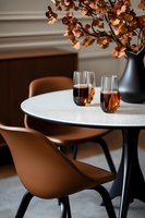 Modern dining setup with round white table, brown chairs, wine glasses and autumn leaves in black vase creating elegant atmosphere for restaurant interior design.