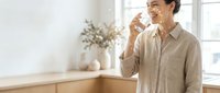 Young Asian man drinking fresh water from glass in bright modern kitchen with natural lighting and minimalist decor for healthy lifestyle concept.