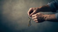 Male hands holding vintage brass key against moody dark background with dramatic lighting for real estate and security concepts.
