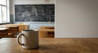 White ceramic coffee mug on wooden desk in empty classroom with blackboard and school benches creating educational atmosphere for morning break.