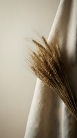 Dried wheat bundle tied with natural linen fabric against neutral beige background creating rustic farmhouse aesthetic for home decor and styling projects.