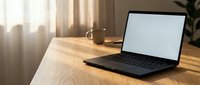 Modern laptop with blank white screen on wooden desk in bright home office workspace with natural sunlight and coffee mug for remote work productivity.