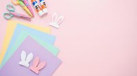 Colorful craft supplies with paper bunny ears on pastel pink background for Easter DIY projects and creative activities.
