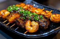 Grilled shrimp and beef skewers glazed with sweet Asian sauce, garnished with green onions and sesame seeds on black ceramic plate, close up food photography.
