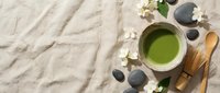 Matcha green tea ceremony setup with bamboo whisk, wooden spoon, stones and white flowers on neutral linen background for wellness and mindfulness concepts.