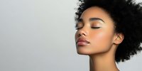 Young African American woman with natural afro hair and glowing skin in profile view against neutral gray background, showcasing natural beauty and minimalist aesthetic.