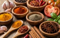 Colorful spices and herbs in wooden bowls with fresh vegetables on rustic table for cooking and seasoning culinary preparations.
