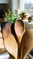 Wooden kitchen utensils in rustic farmhouse kitchen with natural sunlight and green plants creating cozy cooking atmosphere for culinary preparation.