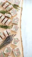 Handmade natural soap bars with marbled pink and green swirls arranged on wooden surface with dried lavender and thyme herbs for spa and skincare products.