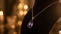 Elegant amethyst teardrop pendant necklace displayed on dark fabric with warm golden bokeh lights in background, suitable for jewelry marketing and luxury product photography.