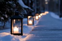 Glowing lanterns illuminate snowy wooden pathway creating warm atmospheric winter evening scene with soft bokeh lights in background.