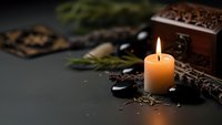 Spa wellness scene with burning candle, hot stones, wooden chest and natural elements creating peaceful relaxation atmosphere for massage therapy.