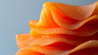 Fresh orange citrus peel macro with detailed texture showing natural curves and layers, bright vibrant color against soft blue background.