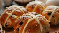 Fresh baked hot cross buns with golden glaze and white icing crosses, traditional Easter pastry with raisins and spices for holiday baking and seasonal treats.