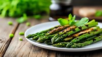 Grilled green asparagus spears seasoned with herbs and spices on white ceramic plate against rustic wooden background, fresh spring vegetables for healthy eating.