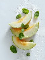 Fresh melon slices with mint leaves on white background, sprinkled with powdered sugar. Refreshing summer food styling for culinary content.