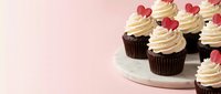 Chocolate cupcakes with vanilla frosting and red heart decorations on white plate against soft pink background for Valentine's Day celebration.