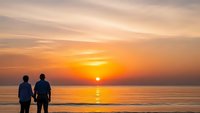 Two people silhouettes watching golden sunset over calm ocean water with orange sky reflection on beach for romantic vacation travel concept.