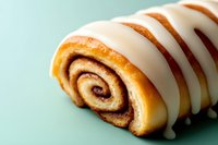 Fresh cinnamon roll with white icing drizzle on mint green background. Sweet pastry dessert for bakery menu, food blog, recipe card design.