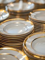 Elegant white porcelain plates with gold trim stacked in multiple piles, creating a luxurious table setting for fine dining and special occasions.