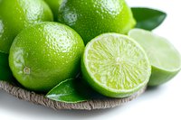 Fresh ripe limes with green leaves on woven plate against white background, one cut in half showing juicy pulp segments, close up view for food and drink designs.