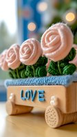 Delicate pink ribbon roses arranged in wooden box with love text, green fabric leaves, and soft bokeh lights in background, creating romantic composition.