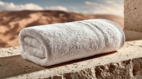 Soft white towel folded on stone ledge with desert landscape background. Spa relaxation and luxury hotel amenities concept for wellness and hospitality design.